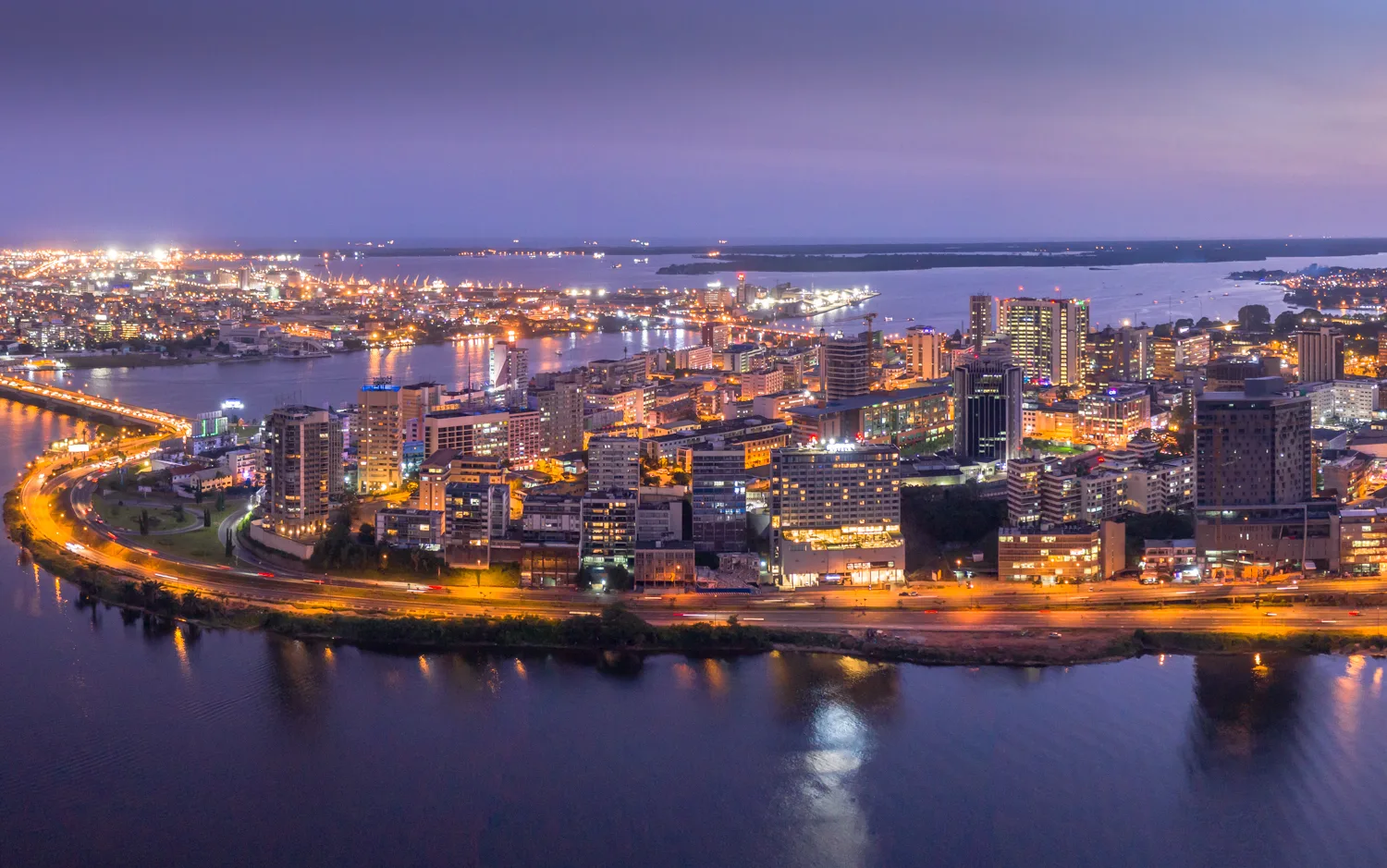 Africa photo — Vue aérienne nocturne d'une ville portuaire dynamique, où des gratte-ciels et bâtiments bien éclairés bordent un fleuve aux reflets ble