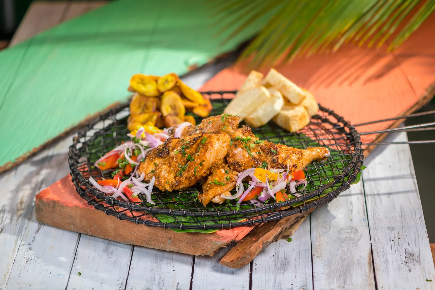 Africa photo — Un plat de poulet grillé et assaisonné, posé sur une grille en métal posée sur un support en bois, accompagné de tranches de bananes pl