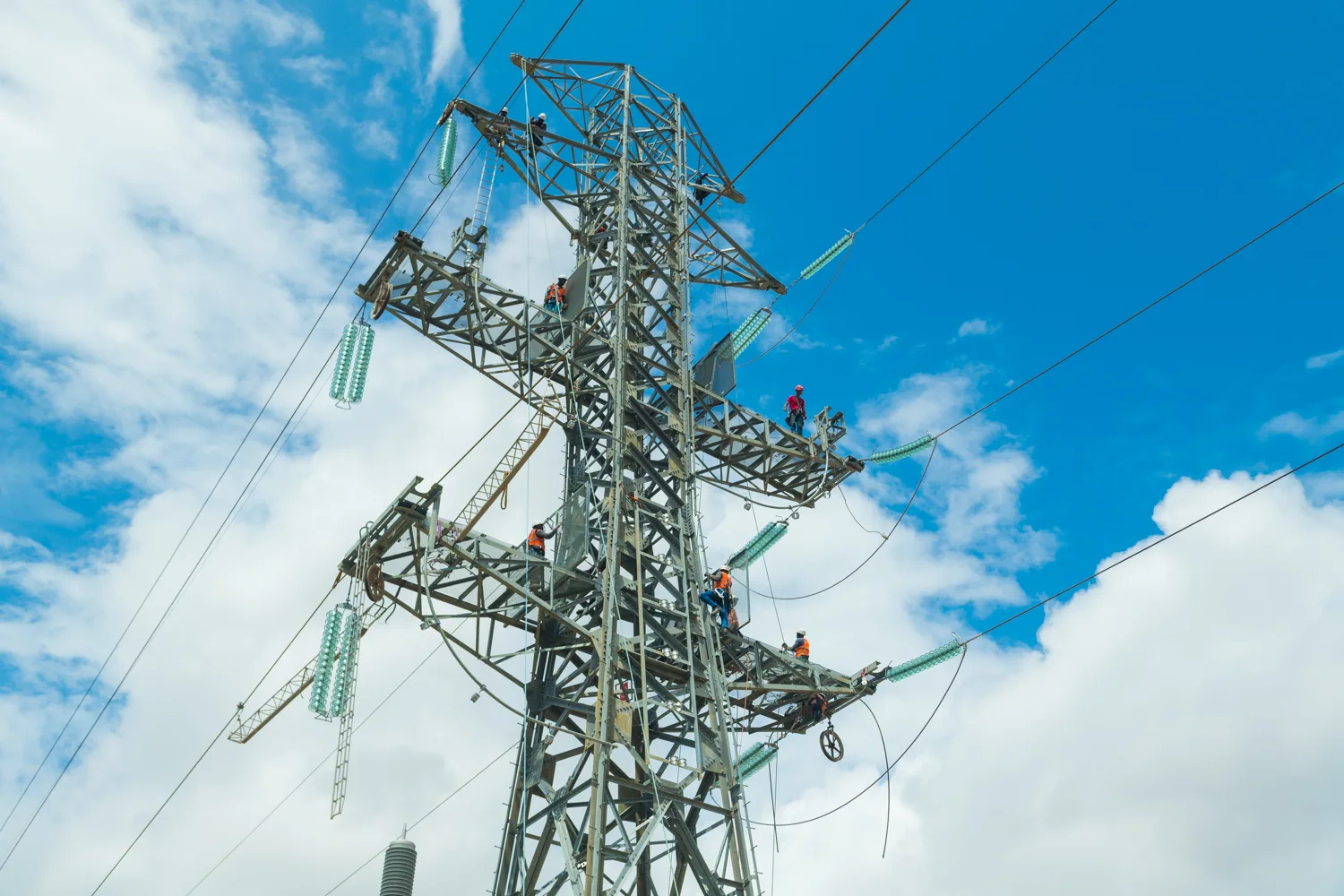 Africa photo — Quatre techniciens équipés de harnais de sécurité interviennent sur une structure métallique complexe de ligne électrique haute tension