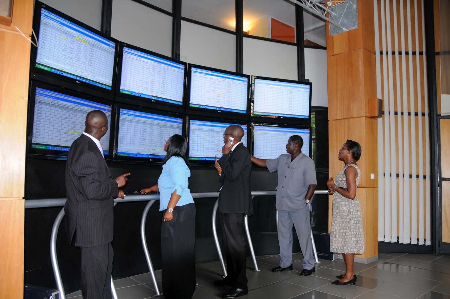 Africa photo — Cinq professionnels debout autour d’un ensemble de six écrans affichant des données techniques, discutant et analysant des informations