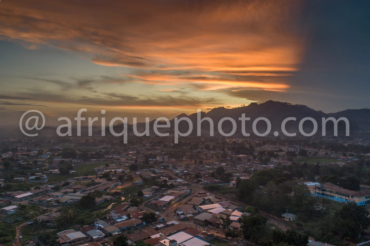Africa photo — Vue aérienne d’une ville africaine baignée par les dernières lueurs du coucher de soleil, avec des maisons aux toits colorés et une mon