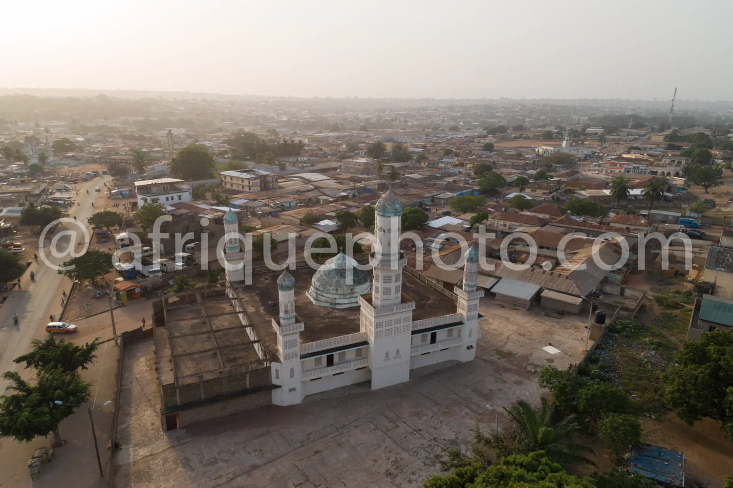 Africa photo — Vue aérienne d’une mosquée blanche avec deux minarets et un dôme bleu, entourée de maisons et de rues animées dans une ville africaine