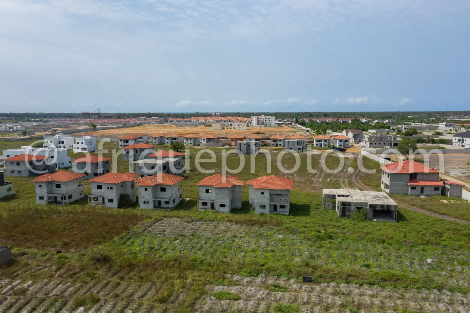 Africa photo — Vue aérienne d’un quartier en construction avec plusieurs maisons en béton aux toits orange, entourées de terrains en terre et de zones