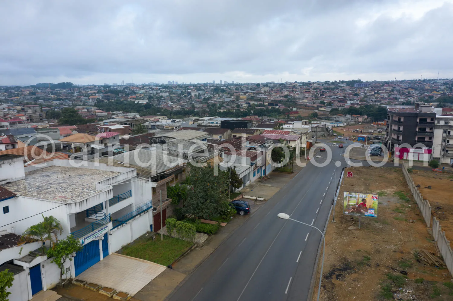 Africa photo — Une vue aérienne d’un quartier résidentiel en développement, montrant une route principale asphaltée bordée de maisons et d’immeubles d