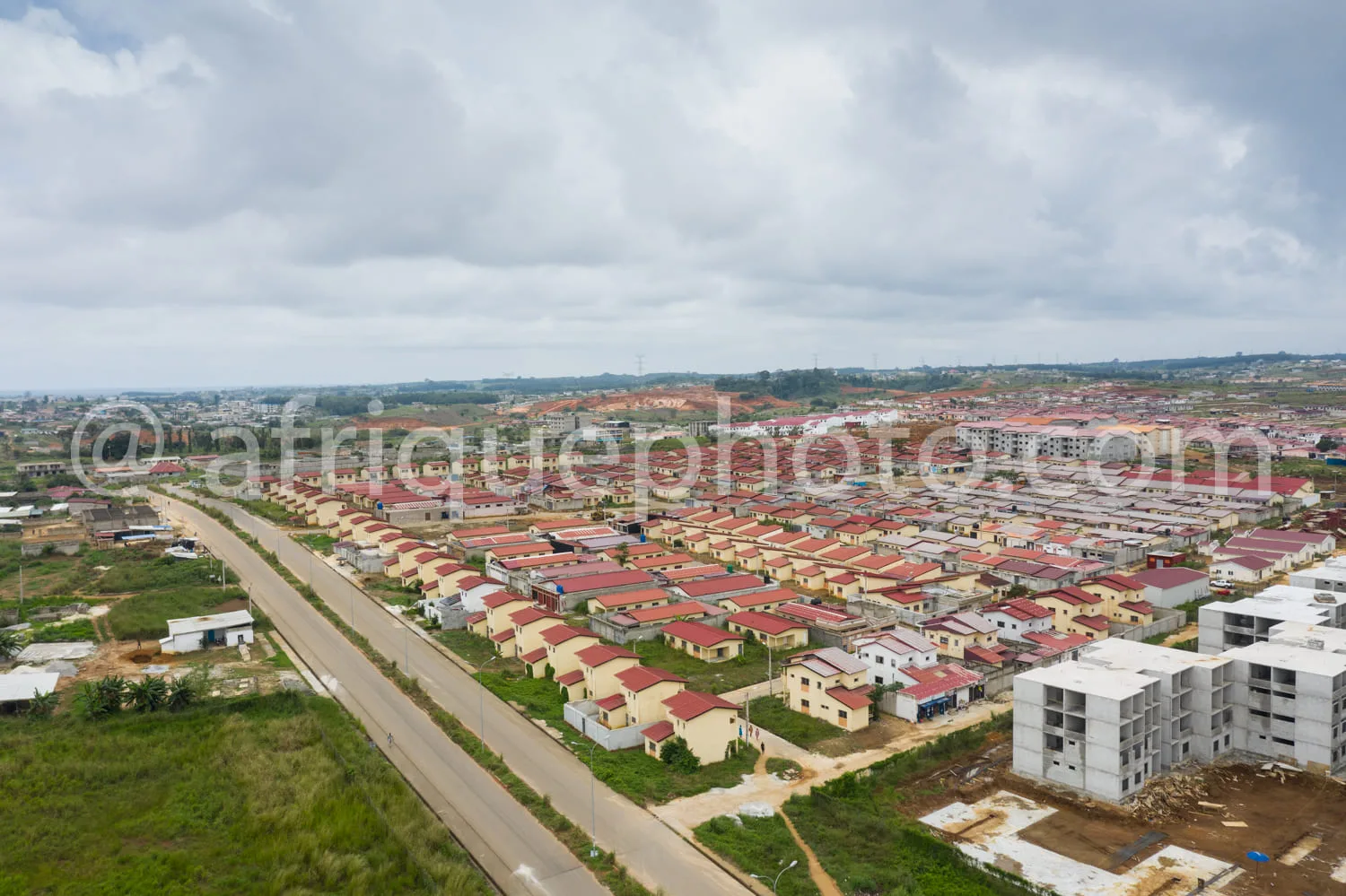 Africa photo — Vue aérienne d’un quartier en développement avec des rangées de maisons individuelles aux toits rouges, une large route centrale et des