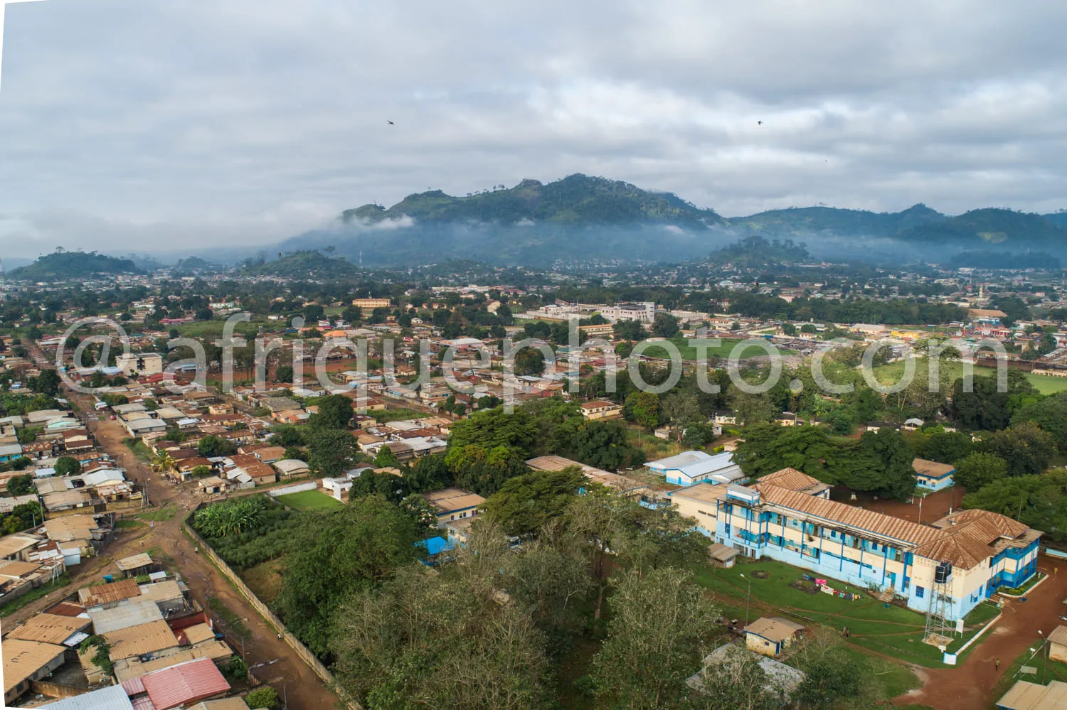 Africa photo — Une vue aérienne d'une ville africaine entourée de montagnes partiellement couvertes de nuages. On aperçoit des habitations de tailles