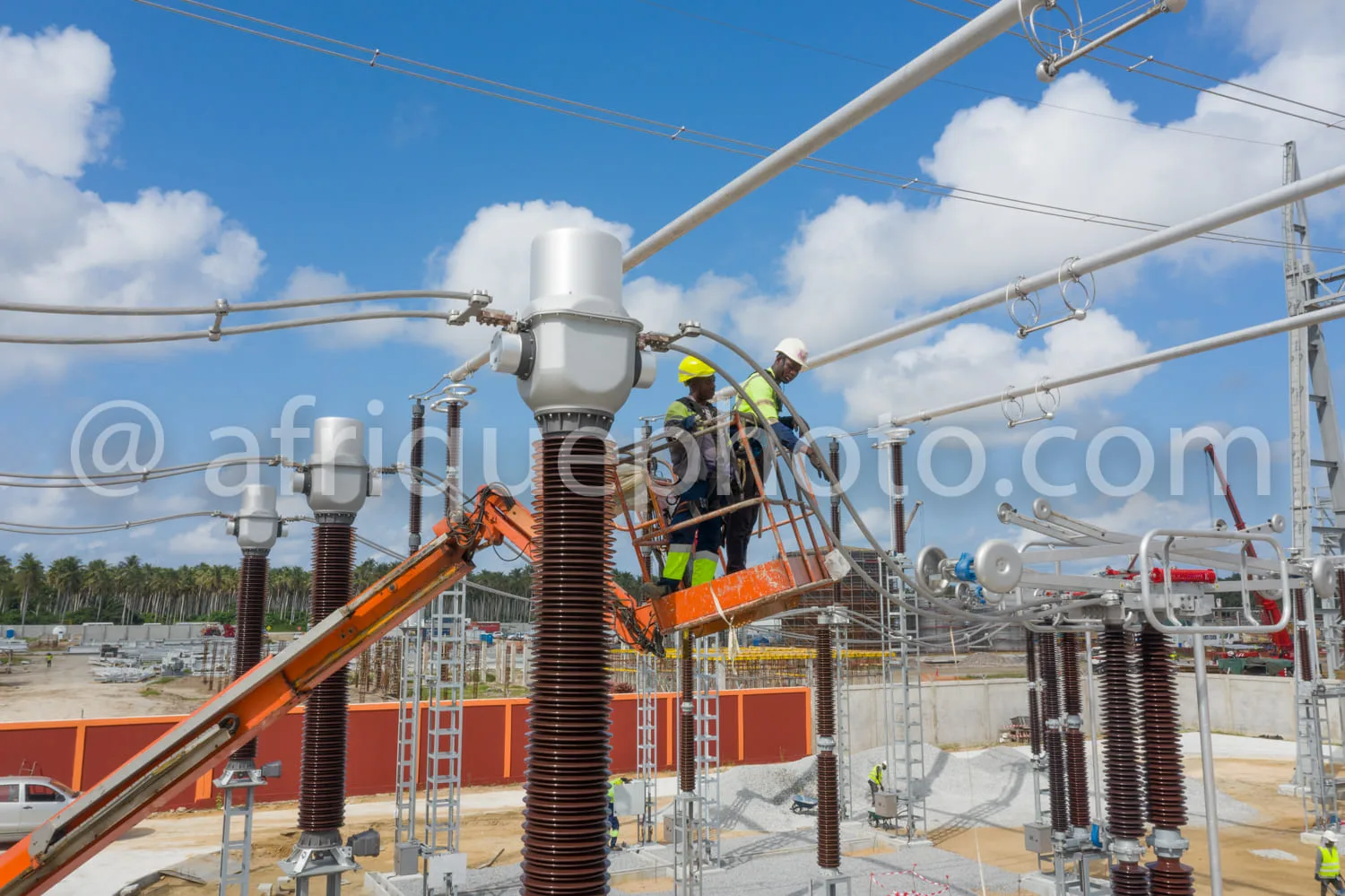 Africa photo — Deux techniciens en combinaison de travail et casques de sécurité effectuent des opérations de maintenance sur un poste électrique haut