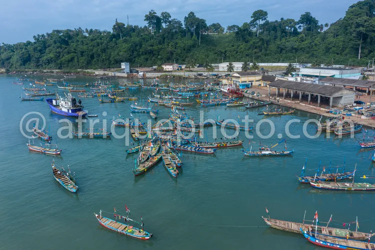 Africa photo — Vue aérienne d’un port de pêche animé où des dizaines de bateaux traditionnels aux couleurs vives sont amarrés le long d’un quai en boi