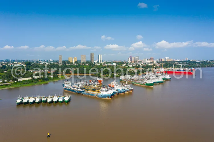 Africa photo — Vue aérienne d’un port maritime où plusieurs navires de différentes tailles sont amarrés le long des quais. En arrière-plan, une ville