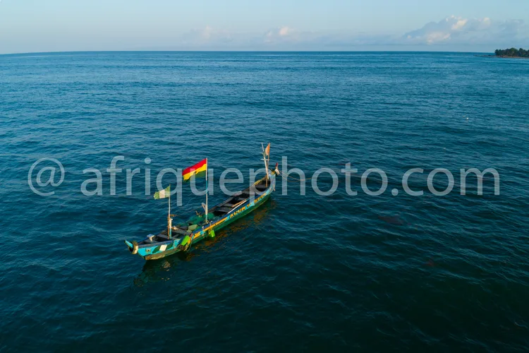 Africa photo — Une pirogue peinte aux couleurs vertes, bleues et rouges flotte calmement sur une étendue d'eau bleue, avec un drapeau à trois bandes v