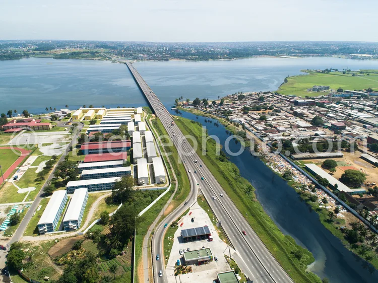 Africa photo — Image montrant un long pont traversant une rivière, avec des bâtiments industriels à gauche, une route à plusieurs voies au centre, et
