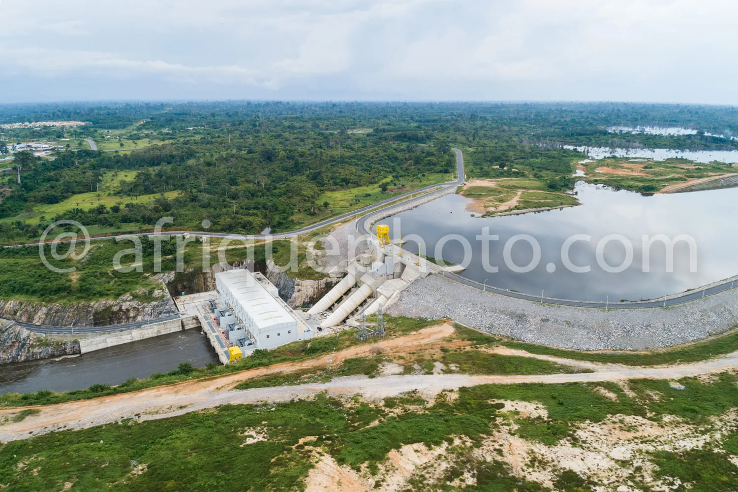 Africa photo — Image aérienne d'un barrage hydroélectrique en construction avec une route sinueuse à gauche, des bâtiments techniques en béton, un rés