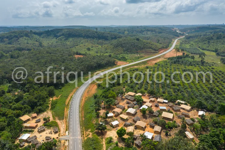 Africa photo — Vue aérienne d'une route sinueuse en bon état traversant un village composé de petites maisons en matériaux locaux, entourée de colline