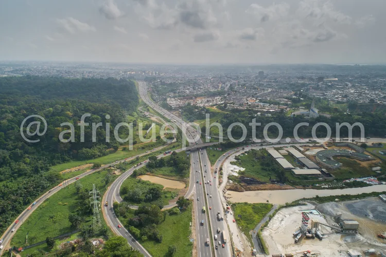 Africa photo — Image montrant une autoroute sinueuse avec plusieurs voies, entourée de zones boisées et de zones urbaines en développement, incluant d