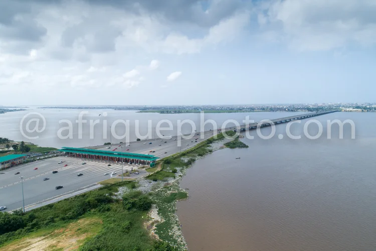 Africa photo — Image montrant une vue aérienne d’un parking couvert rempli de voitures, bordé par une route menant à un long pont enjambant un fleuve