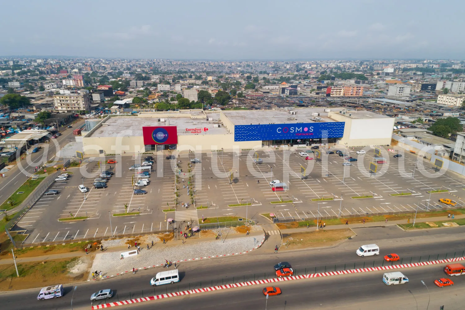Africa photo — Vue aérienne d'un grand centre commercial nommé Cosmos, avec un vaste parking presque vide, des enseignes Carrefour Market et Cosmos bi