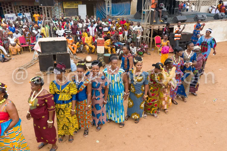Africa photo — Un groupe de femmes vêtues de robes traditionnelles africaines aux motifs bleus, jaunes et rouges, ornées de bijoux et coiffures élabor