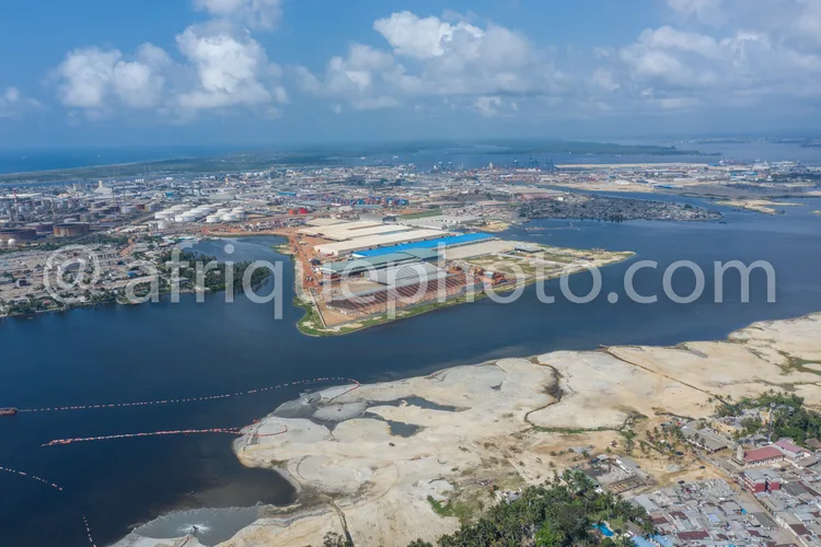 Africa photo — Image aérienne montrant un port industriel avec des quais de chargement, des entrepôts et des zones de stockage en bordure d’un fleuve,