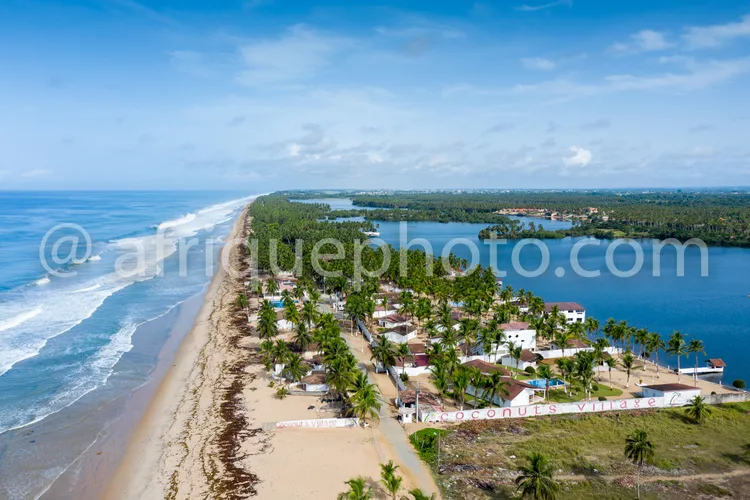 Africa photo — Vue aérienne d’un village côtier paisible bordé d’une plage de sable clair, de palmiers et de maisons colorées, avec une lagune bleue à