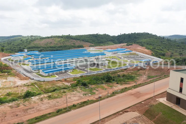 Africa photo — Vue aérienne d'une vaste usine aux structures blanches et toits bleus, entourée de végétation et de terrains en terre, avec une route d