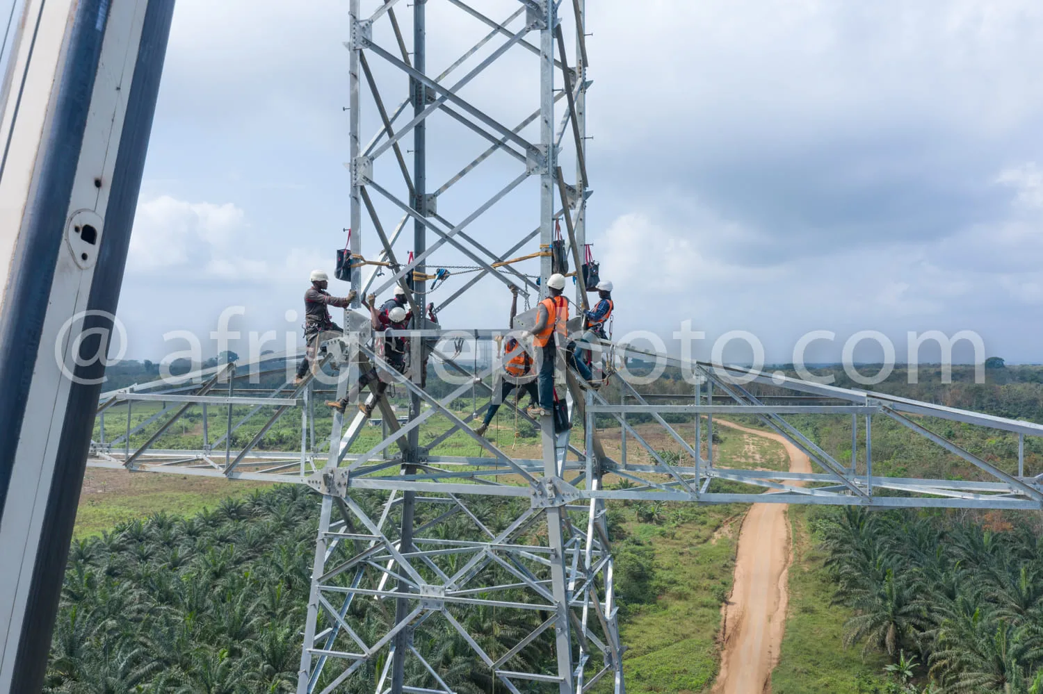 Africa photo — Quatre techniciens en combinaison de travail et casque de sécurité montent et installent des équipements sur un pylône métallique en ha