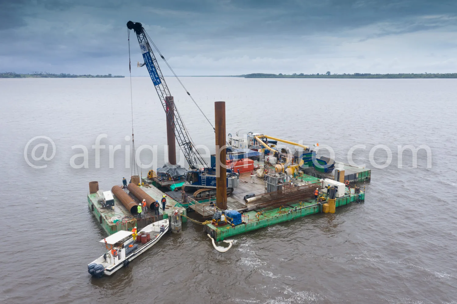 Africa photo — Une barge de travail flottant sur une étendue d'eau avec une grue de levage, des cylindres métalliques et des équipements industriels.