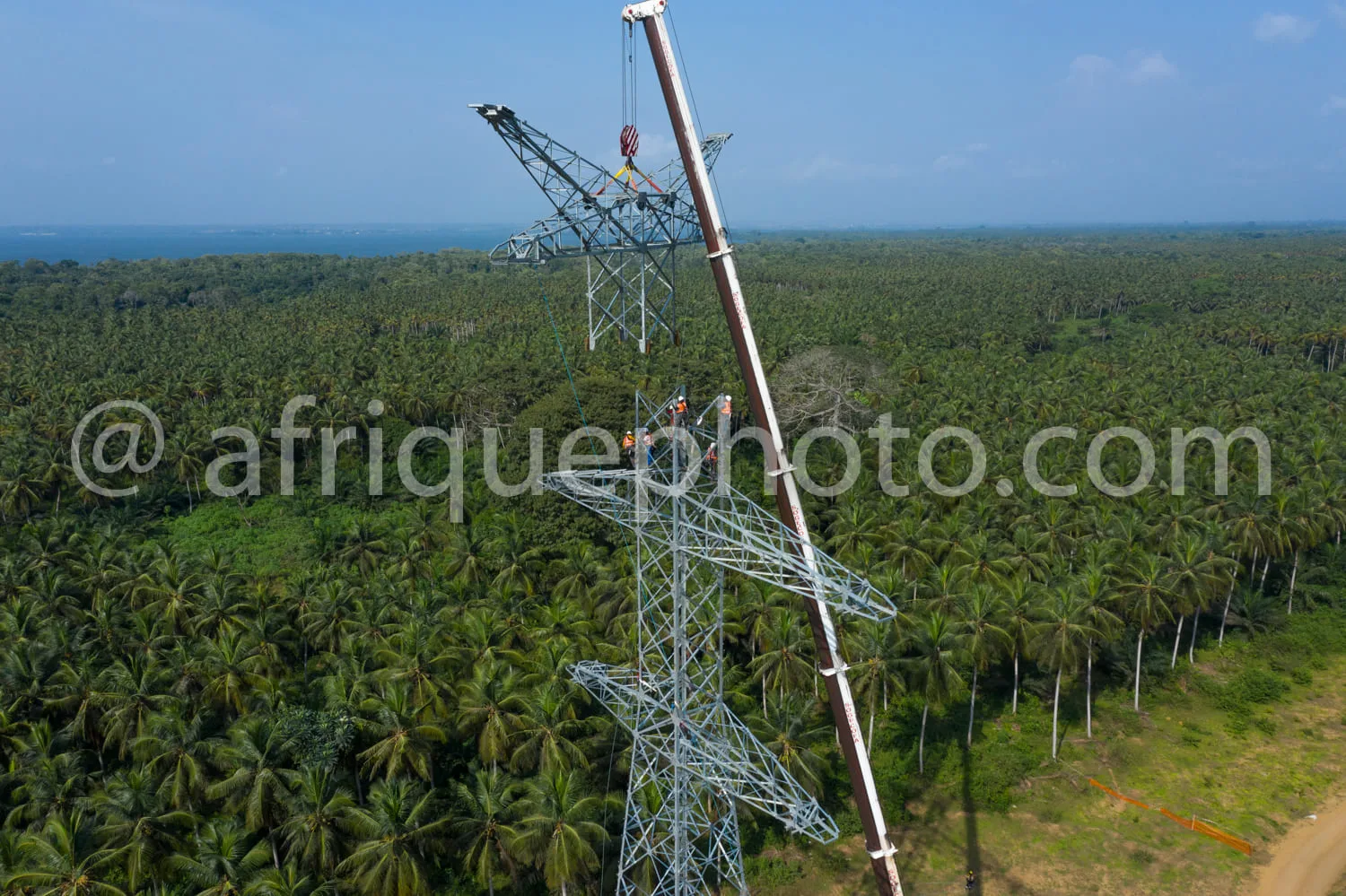 Africa photo — Deux techniciens en équipement de sécurité travaillent sur une tour métallique de ligne électrique haute tension, entourée d’une vaste