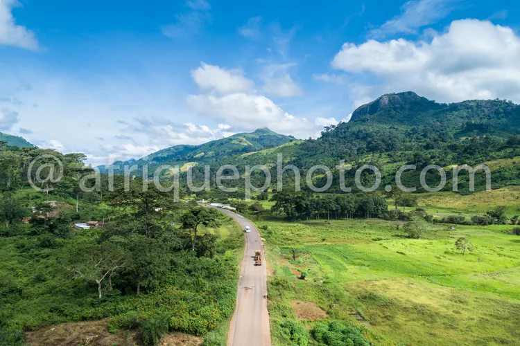 Africa photo — Une route sinueuse bordée de végétation dense traverse une vallée verdoyante sous un ciel bleu légèrement nuageux, avec des montagnes e