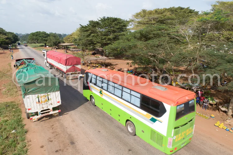 Africa photo — Vue aérienne d’un bus vert et blanc stationné sur une route poussiéreuse, entouré de deux camions couverts de bâches rouges et vertes,