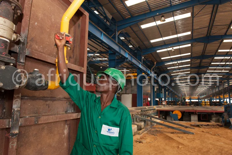 Africa photo — Un technicien industriel portant un casque de sécurité vert et une combinaison verte manipule une vanne jaune et rouge fixée à une stru