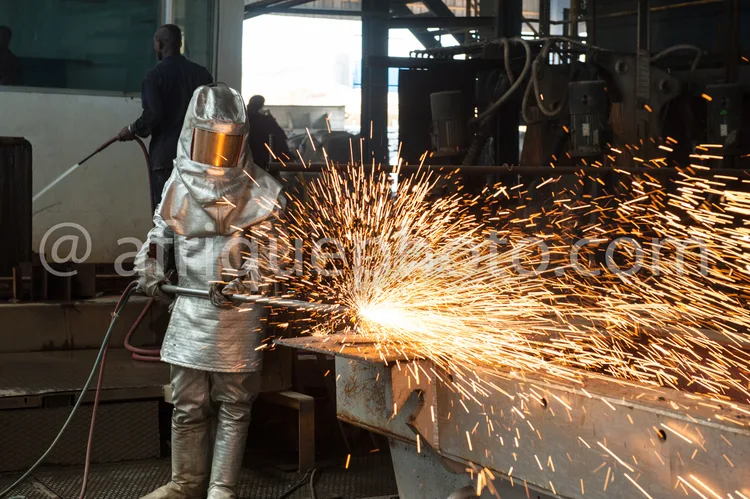 Africa photo — Un soudeur équipé d'une combinaison protectée en métal et d'un masque soudeur travaille dans un atelier industriel. Des étincelles jail