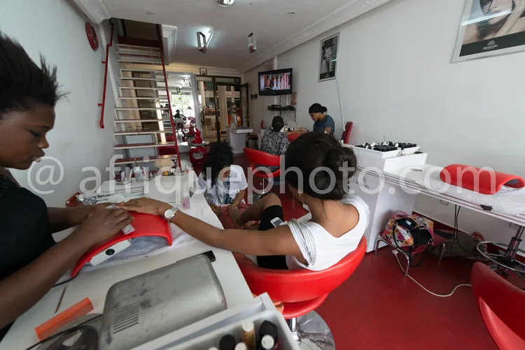 Africa photo — Trois coiffeuses travaillent assidûment dans un salon moderne. On entend le bruit des sèche-cheveux et des discussions, avec des fauteu