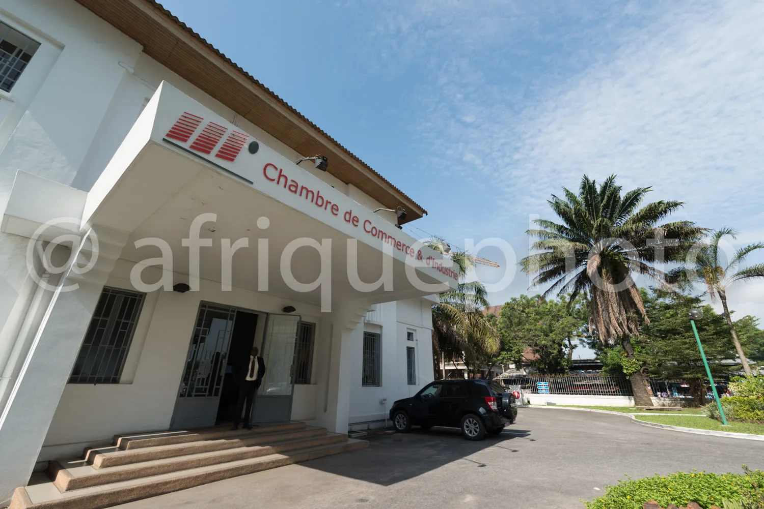 Africa photo — Bâtiment blanc de la Chambre de Commerce et d'Industrie avec un logo rouge et noir en haut de la façade, des portes vitrées et une voit