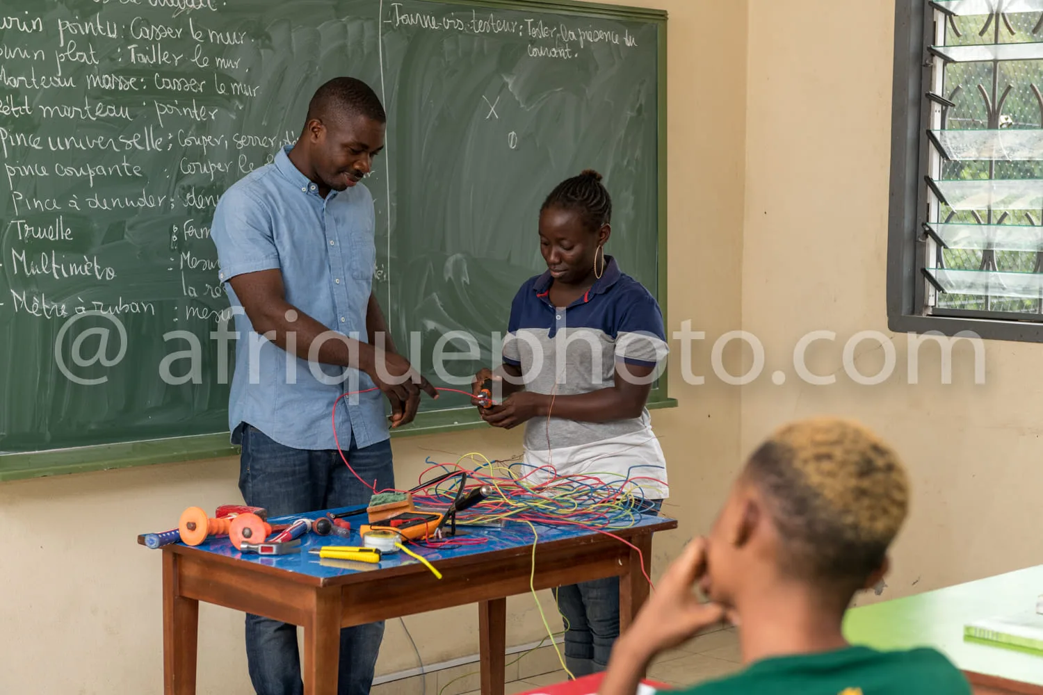 Africa photo — Un professeur et une élève en classe travaillent ensemble sur une table avec des fils électriques colorés, des outils et des pinces, ta