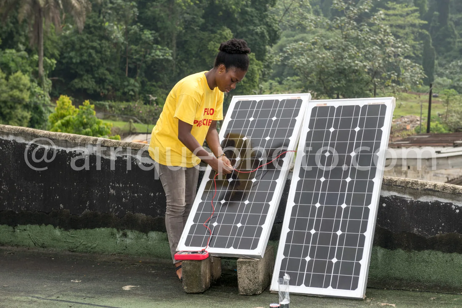 Africa photo — Un technicien en jaune manipule deux grands panneaux solaires noirs et blancs, posés sur un support en béton, dans un environnement ver