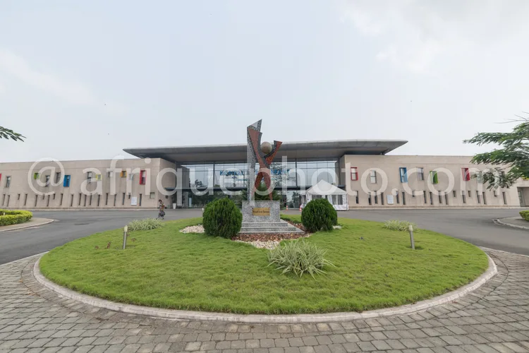 Africa photo — Une statue imposante en forme de silhouette humaine stylisée, érigée sur un socle circulaire au centre d’un rond-point gazonné, entouré