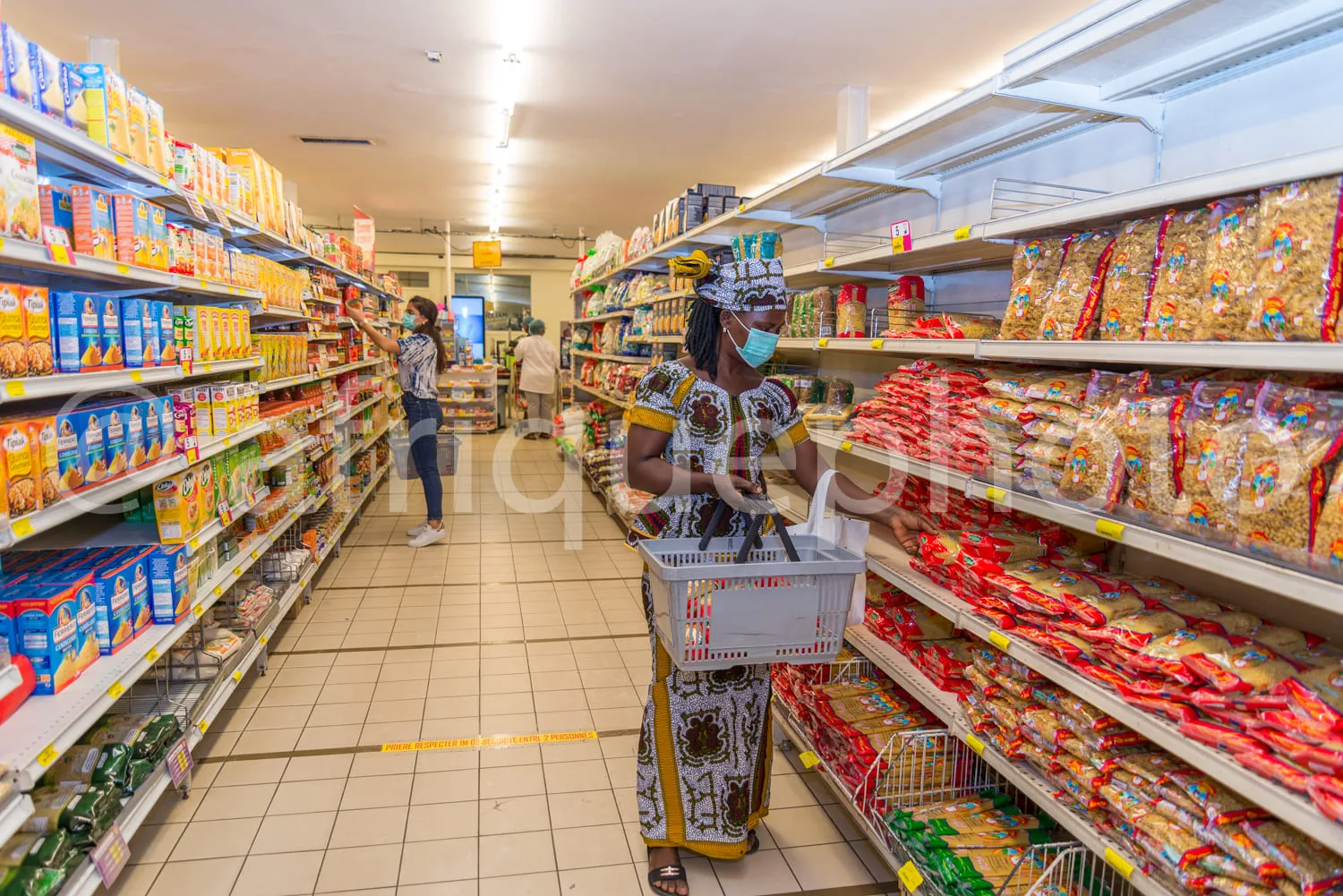 Africa photo — Deux femmes portant des masques se déplacent dans un rayon d'épicerie bien éclairé. L'une pousse un panier rempli de produits tandis qu