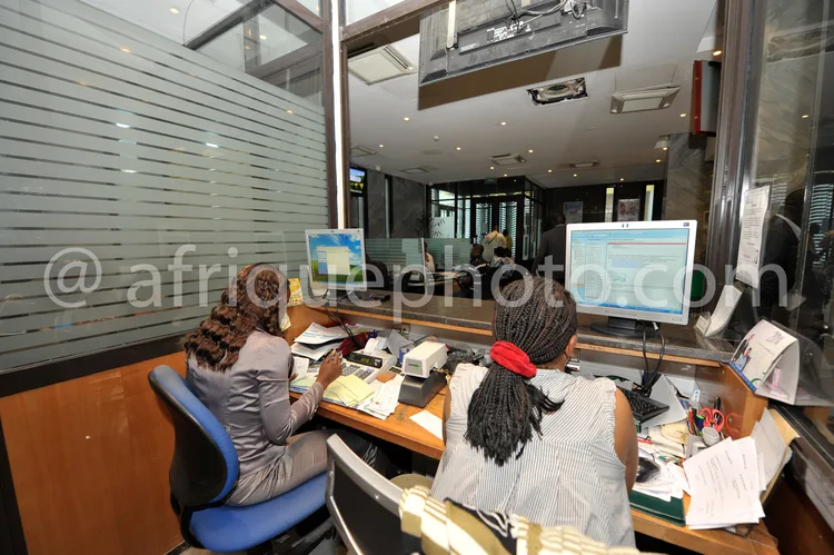Africa photo — Deux personnes assises à des bureaux en bois, chacune devant un écran d'ordinateur allumé affichant des interfaces professionnelles, en