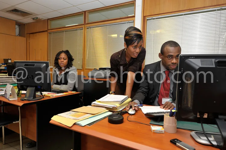 Africa photo — Trois personnes assises autour d’une table de réunion dans un bureau lumineux, travaillant sur des ordinateurs et des documents, en ten