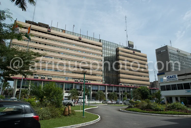 Africa photo — Un grand bâtiment administratif de plusieurs étages, en façade beige clair avec des fenêtres alignées et des balcons. On aperçoit des d