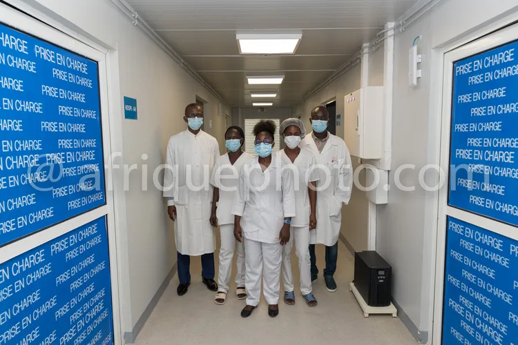 Africa photo — Cinq professionnels de santé souriants, vêtus de blouses blanches et portant des masques chirurgicaux, se tiennent dans un couloir hosp