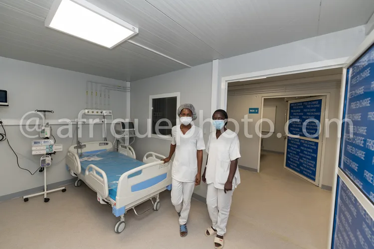 Africa photo — Deux infirmiers en tenue médicale blanche, dont l’un porte une coiffe et un masque, marchent côte à côte dans un couloir d’hôpital prop