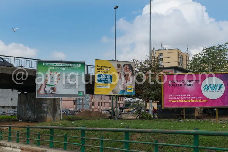 Africa photo — Trois panneaux publicitaires placés près d’un pont et d’un terrain enherbé : le premier annonce une banque digitale, le deuxième promeu