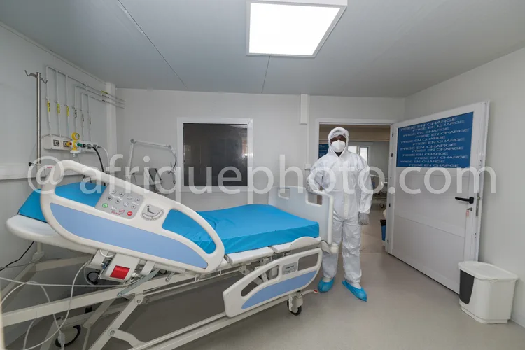 Africa photo — Une pièce médicale aseptisée où un professionnel en combinaison de protection intégrale se tient près d’un lit d’hôpital équipé de disp