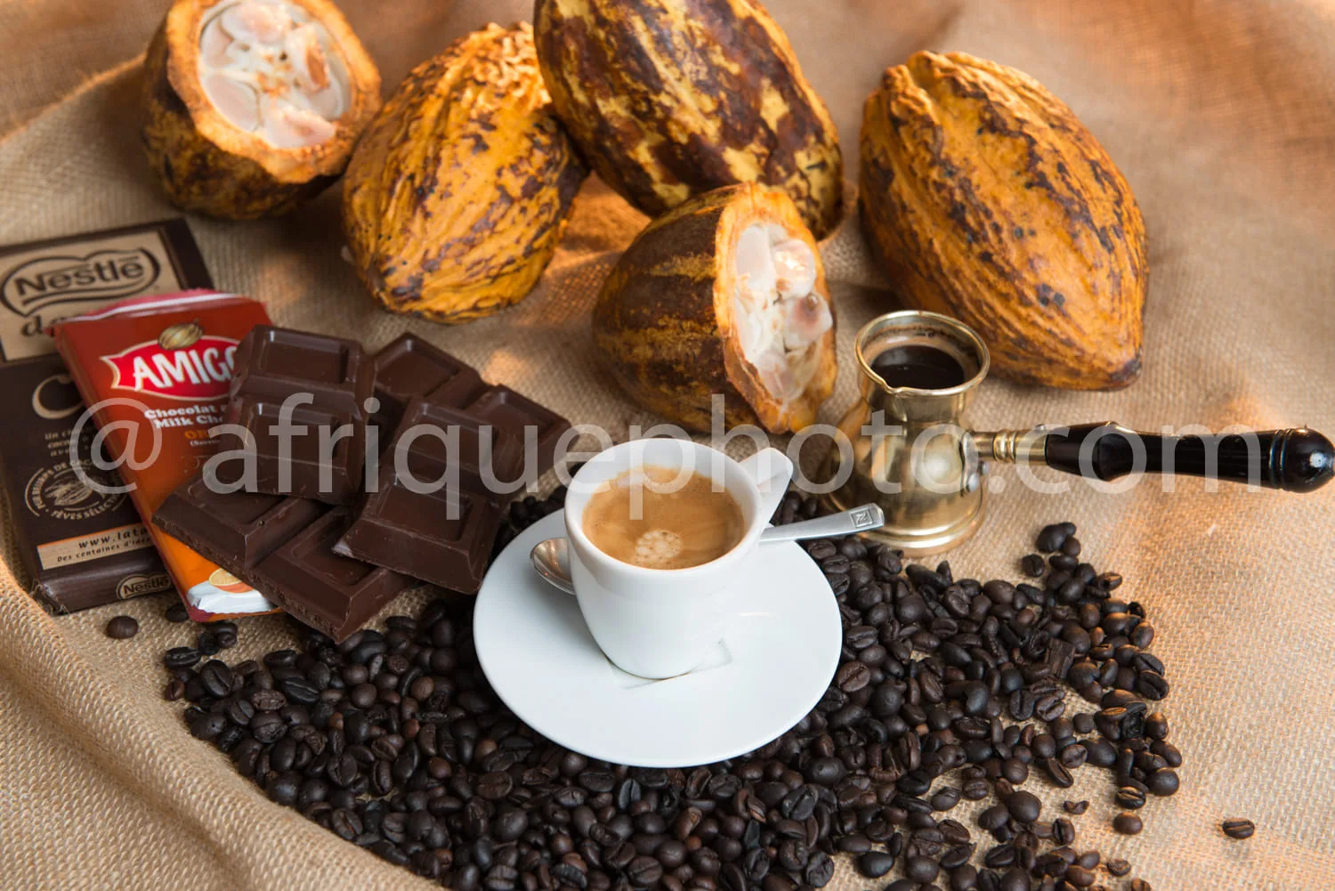 Africa photo — Une scène gourmande montrant trois cabosses de cacao ouvertes révélant leur pulpe blanche, une tasse de café fumant posée sur une souco