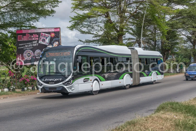 Africa photo — Un bus articulé blanc et vert de la marque Lemergent, modèle Eco, roulant sur une route asphaltée avec des arbres et une signalétique p