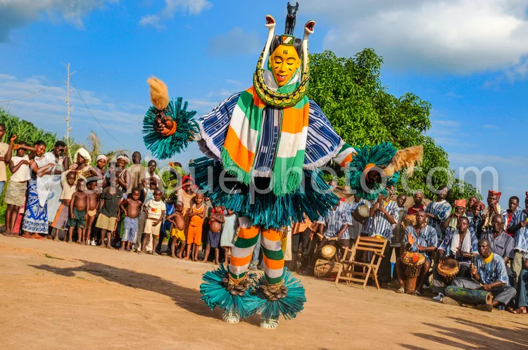 Africa photo — Un danseur vêtu d'un costume traditionnel africain richement décoré, composé de plumes turquoise, de motifs colorés vert, orange et bla
