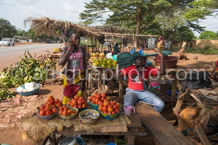 Africa photo — Deux femmes dans un petit étal de marché en plein air, entourées de paniers de fruits frais comme des bananes, des oranges et des anana