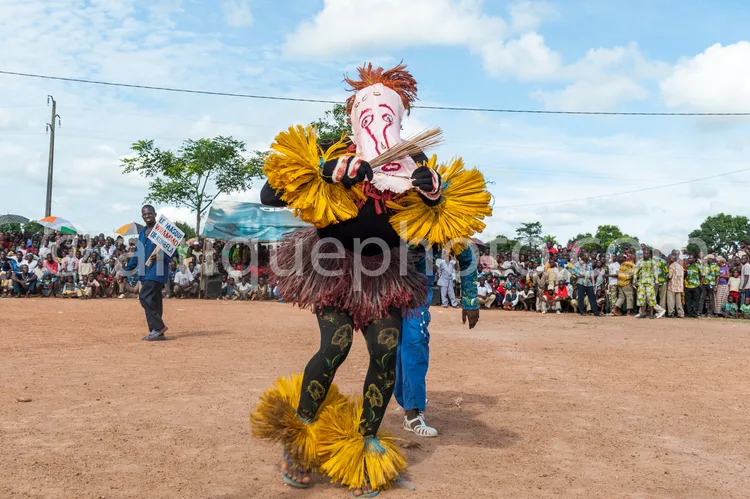 Africa photo — Un danseur vêtu d’un costume traditionnel africain richement décoré de plumes jaunes et de motifs colorés sur les jambes, portant un ma