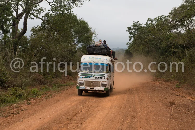 Africa photo — Un véhicule utilitaire Renault Junior, marqué Junior et transportant des passagers sur son toit, roule sur une piste poussiéreuse entou